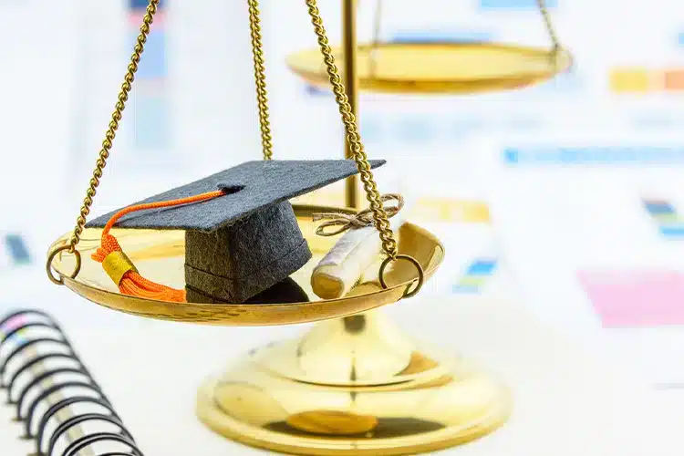  a miniature graduation cap and degree placed in a weighing machine