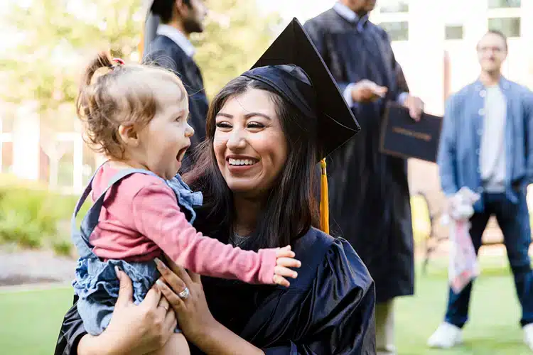 a female college graduate celebrating her graduation with her baby held in her arms