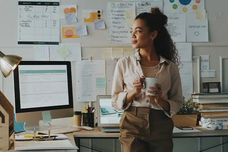 a female corporate employee sipping coffee, standing near her work desk