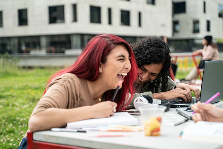 two female college students working together on an assignment and laughing together on a joke someone just cracked