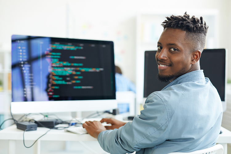 a male college student engaged in coding on his computer screen