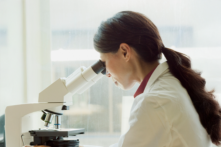 a female scientist investigating a sample under her microscope