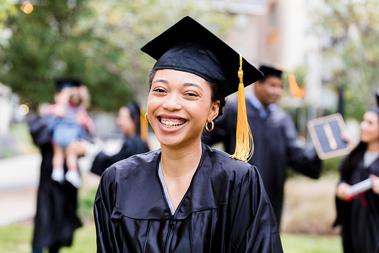 a female American college graduate smiling joyously at her graduation ceremony